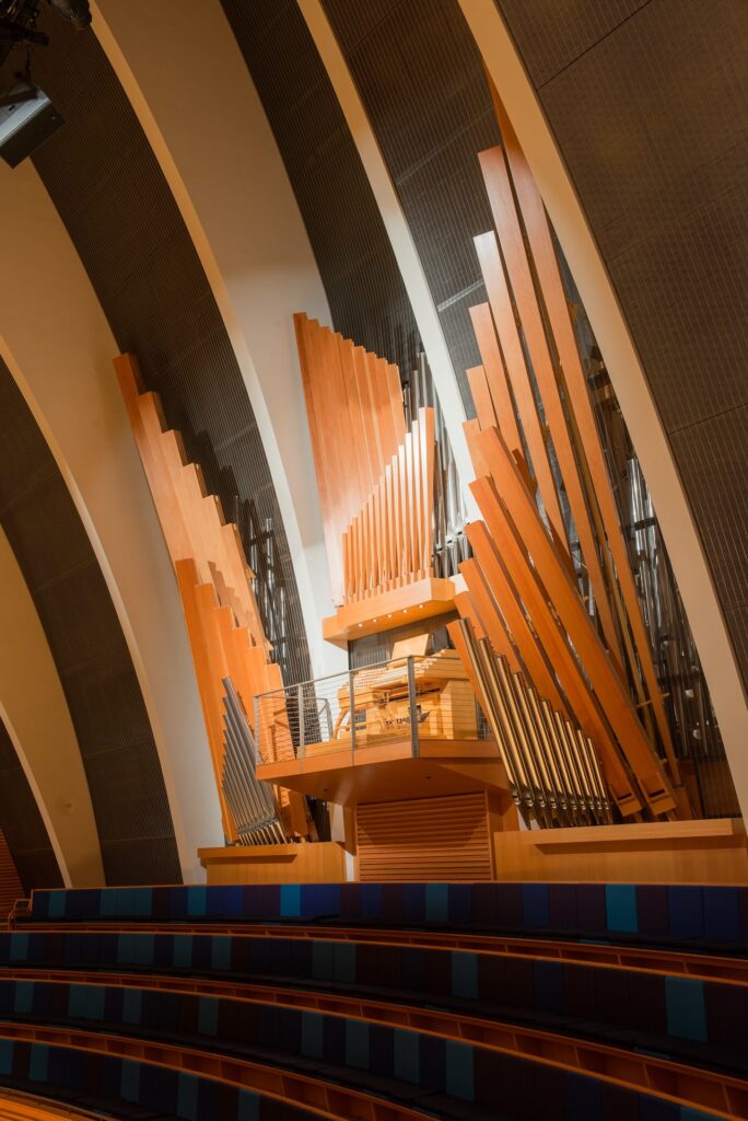 A large pipe organ with wooden pipes is installed in a modern concert hall, featuring curved architectural elements and tiered seating, made possible through generous endowment and legacy gifts.