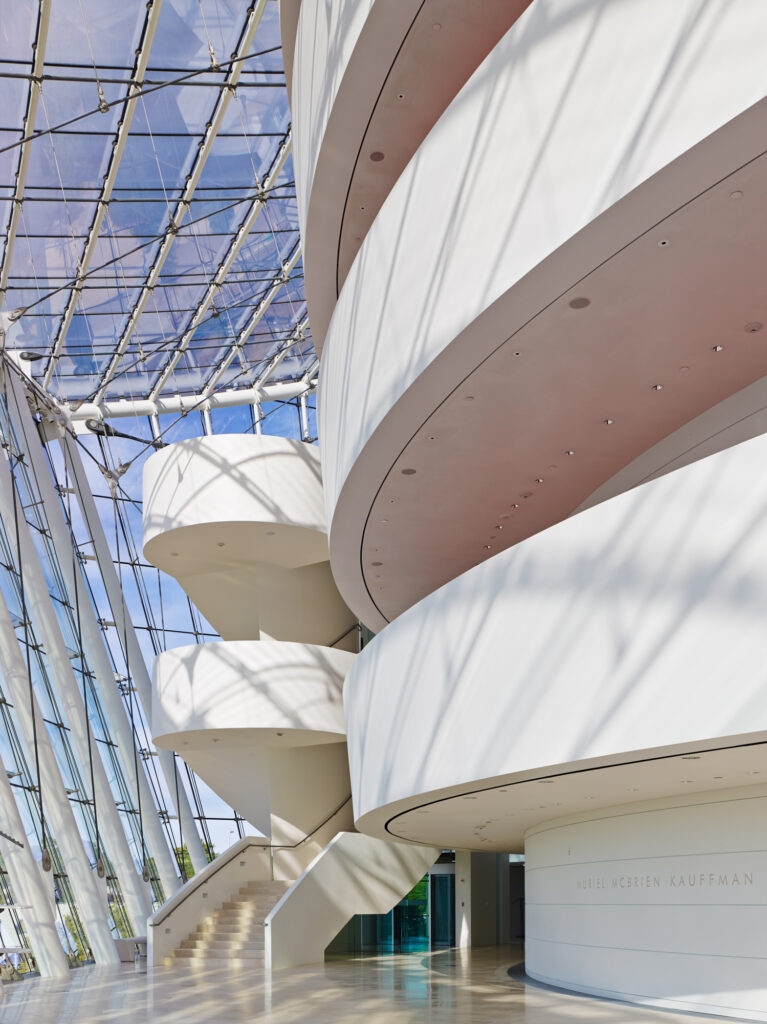 Interior of the Performing Arts Center in Kansas City, featuring modern curved white staircases and a glass roof that lets in abundant natural light.