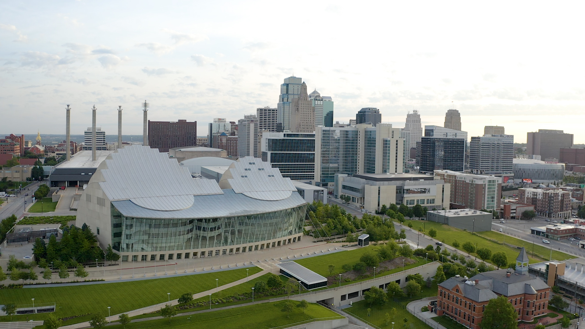 Aerial view of downtown Kansas City, featuring the Kansas City Performing Arts center with its modern building and white roof, surrounded by green spaces and urban architecture.