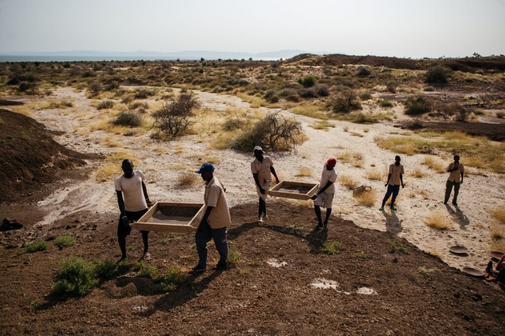 A group of men performing carrying large sifters for paleoanthropology fieldwork.