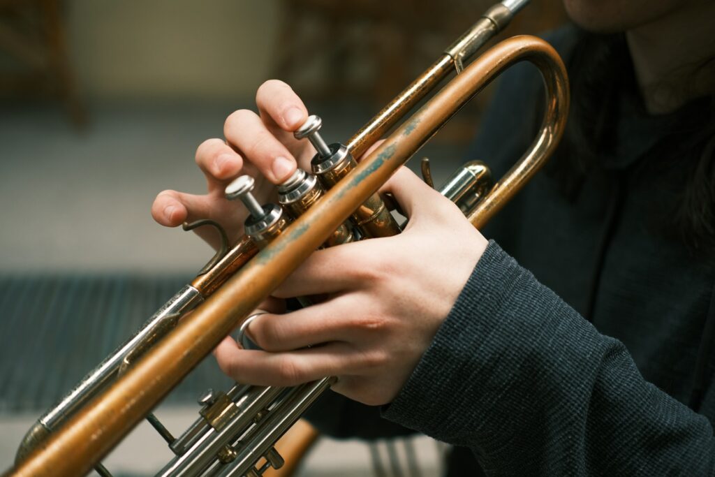 Close-up of a person playing a trumpet, showing their hands pressing the valves on the instrument. The background is blurred, focusing attention on the trumpet and the player's fingers, much like how dining near Kauffman Center offers intimate experiences that highlight culinary details.