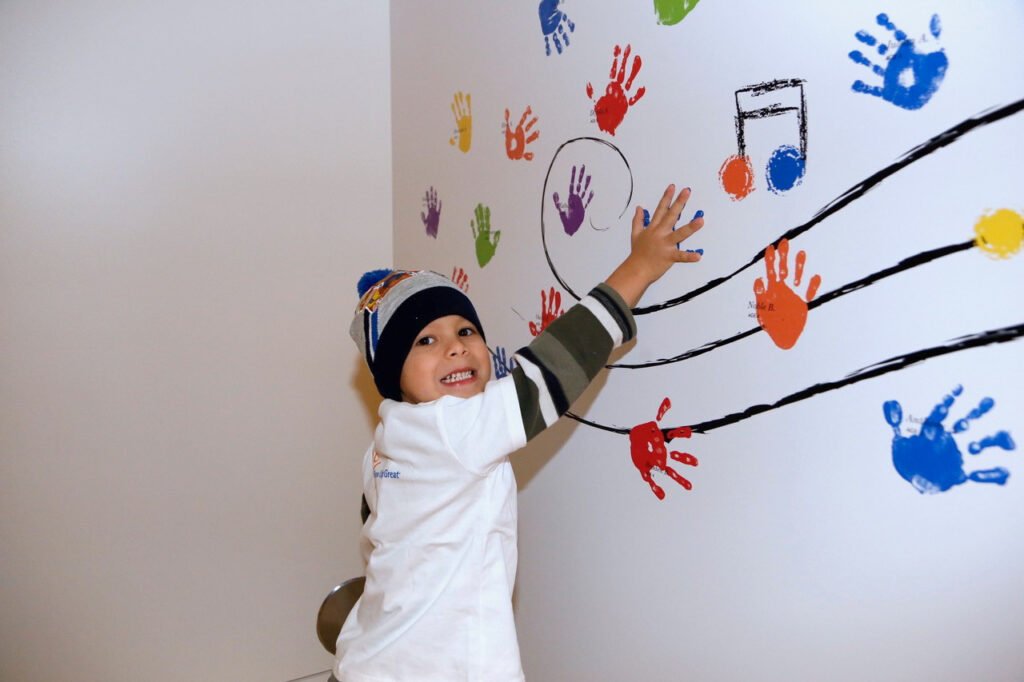 A child touches a wall decorated with colorful handprints and musical notes.